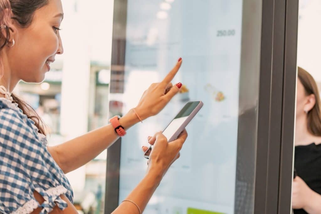 Customer placing an order on a self-ordering kiosk at a quick-service restaurant, where kiosk downtime cost adds up fast